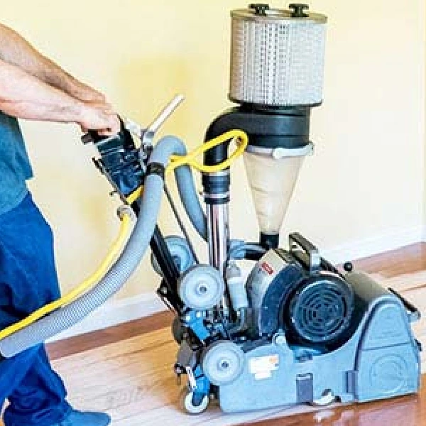 person operating a heavy-duty drum sander on a hardwood floor
