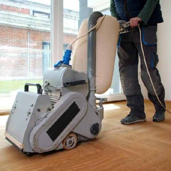 person operating a heavy-duty drum sander on a light wood floor.