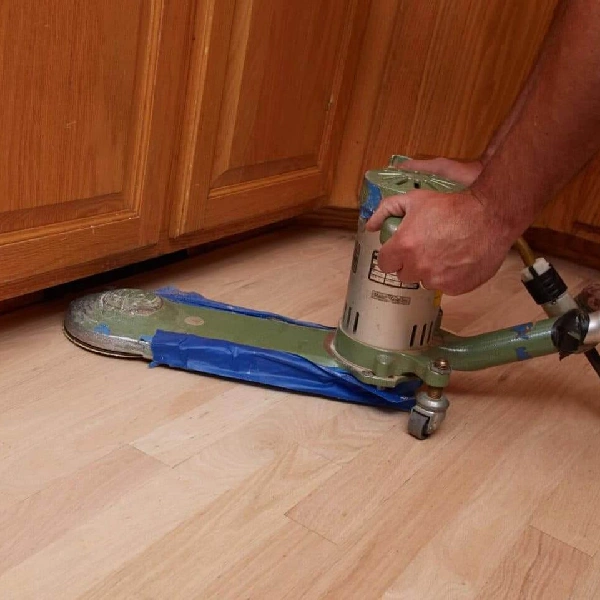 person using an edger sander along the base of wood cabinets