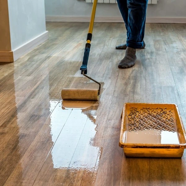 worker applying a glossy solvent-based lacquer to wood floors with a roller